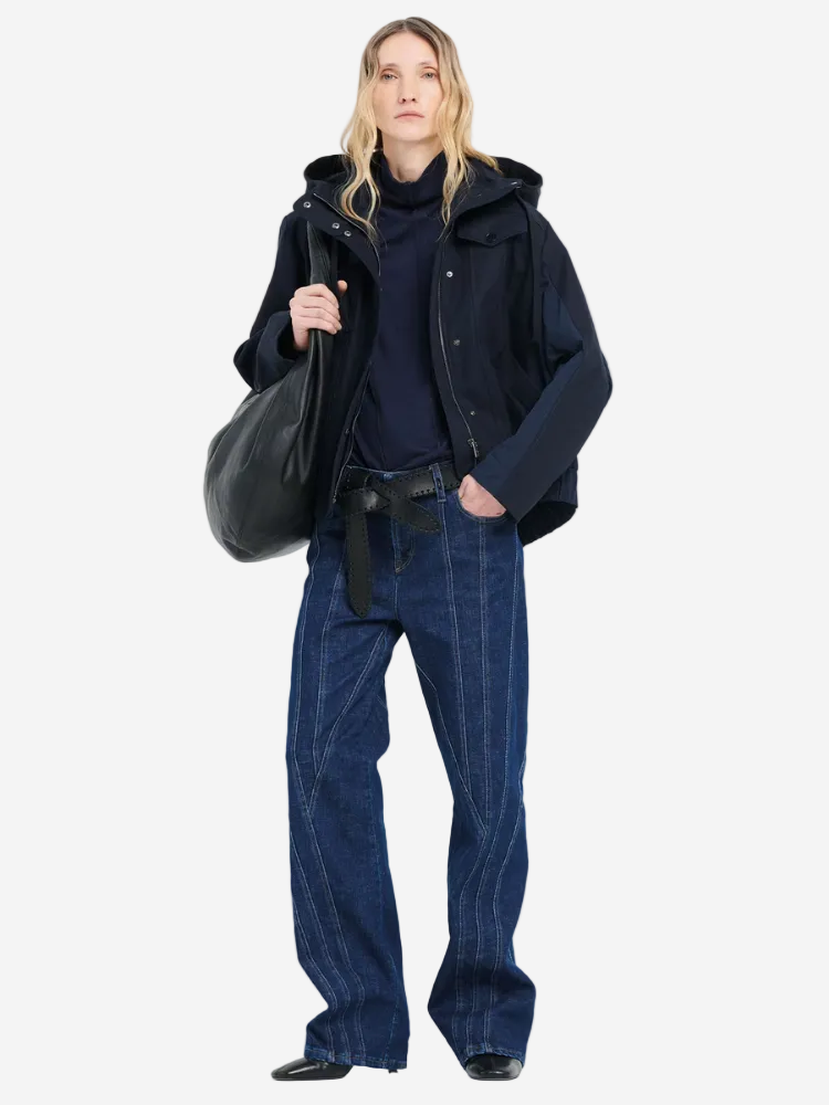 Person wearing a dark coat, black shirt, and blue jeans holding a black bag on a white background