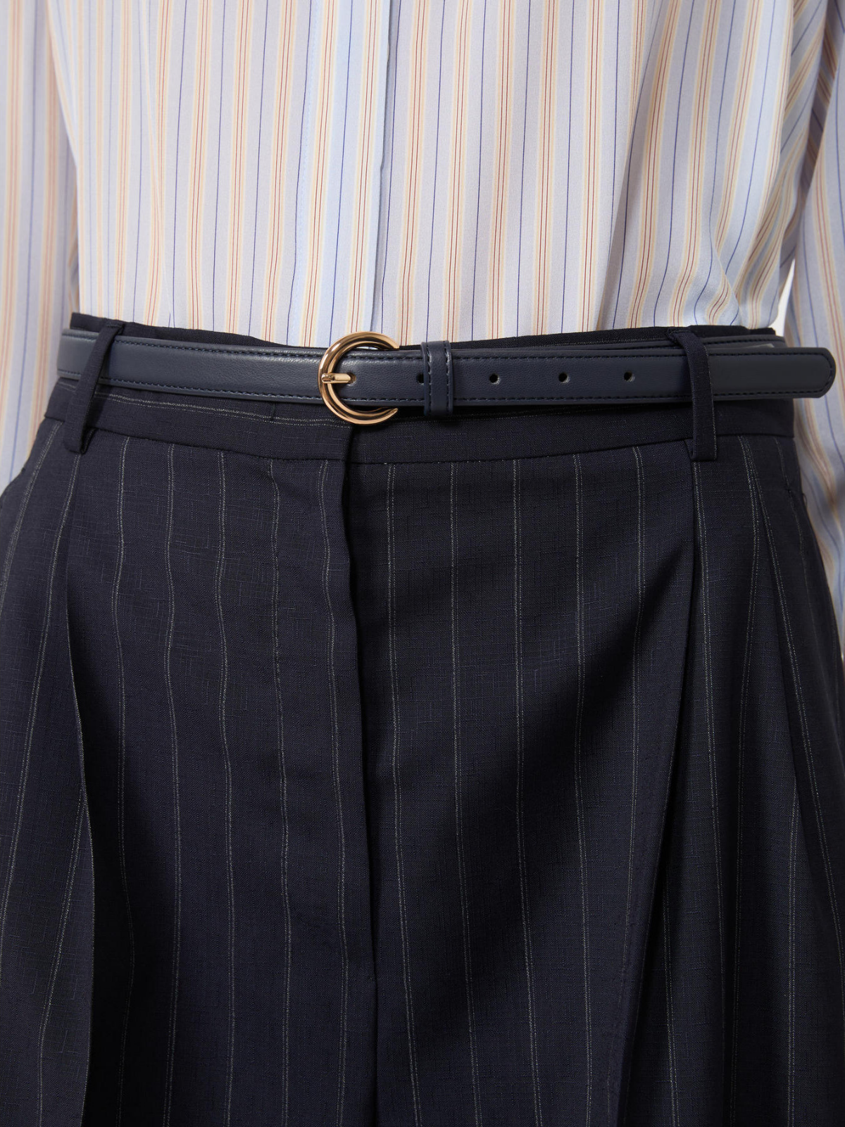 Close-up of a person wearing black pinstripe pants with a black belt and gold buckle, over a striped shirt.
