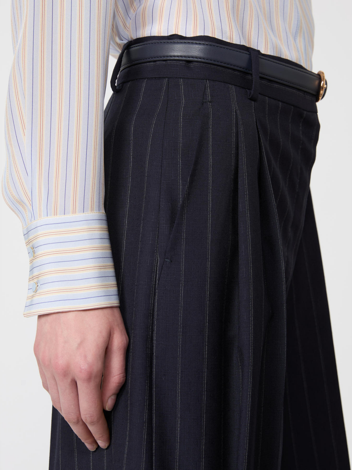 Person wearing a striped shirt and black pinstripe pants with a belt.