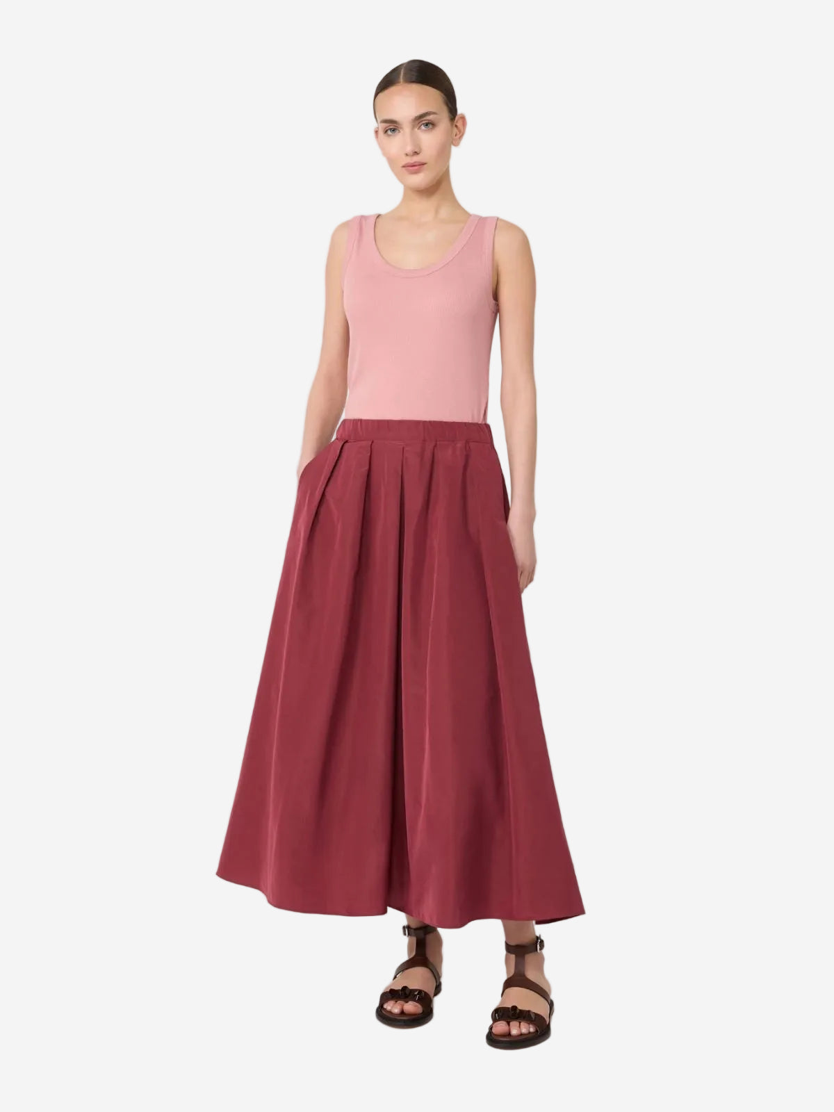 Woman wearing a pink sleeveless top and maroon skirt on a white background