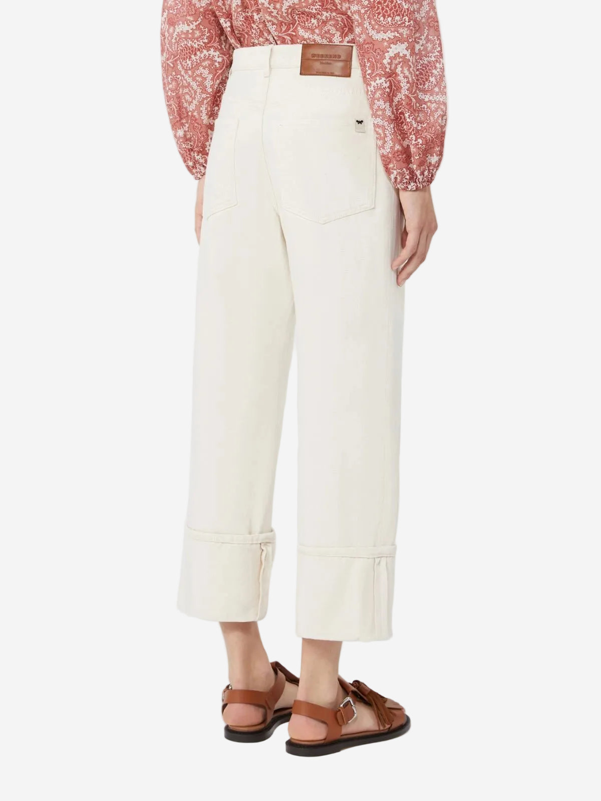 Person wearing a red patterned blouse, white pants, and brown sandals on a white background