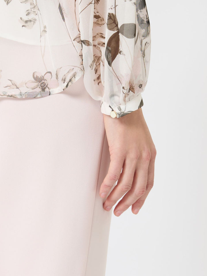 Floral blouse with long sleeves worn by a person, on a plain background