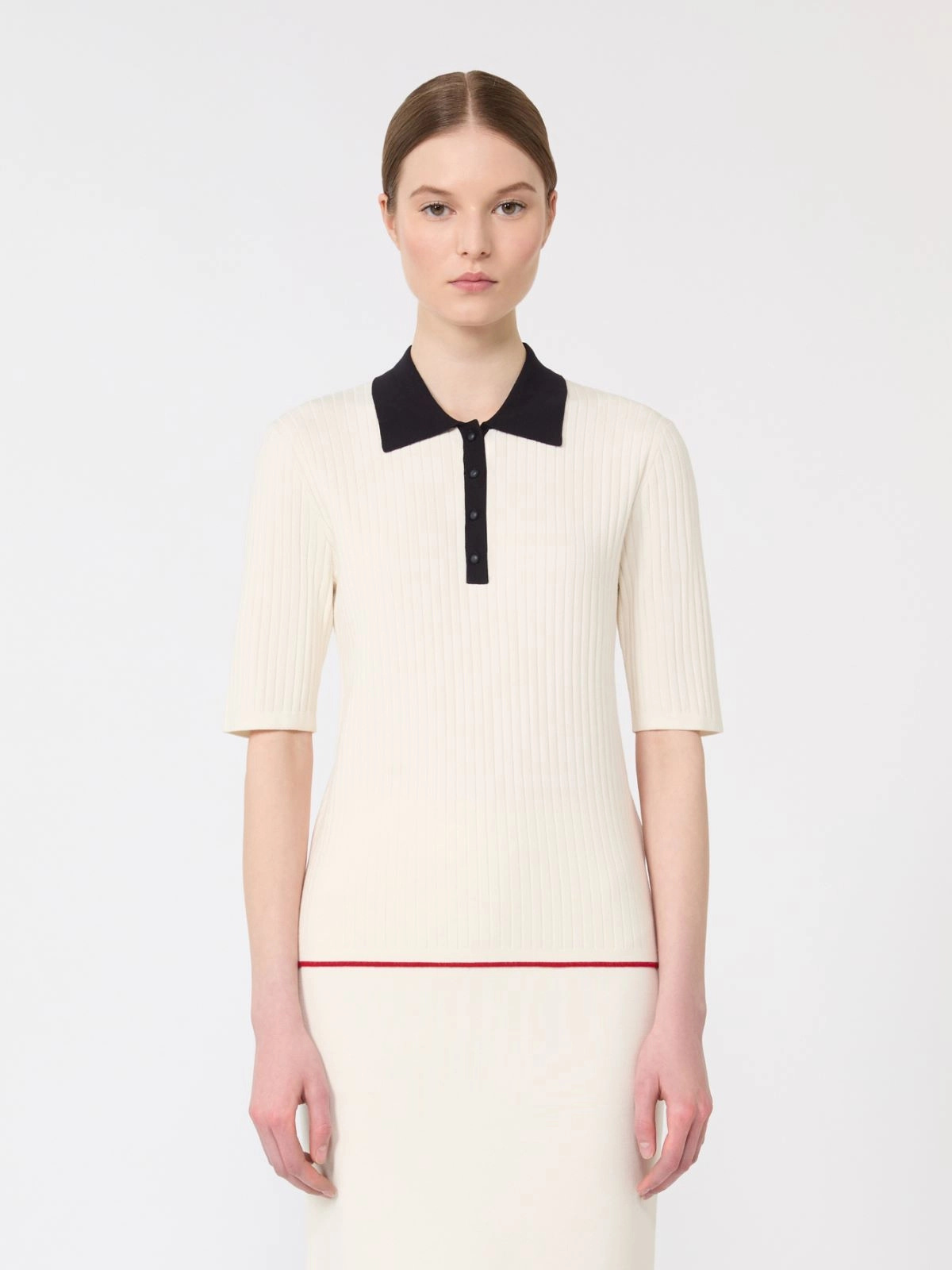 Woman wearing a cream dress with black collar and red trim on a white background