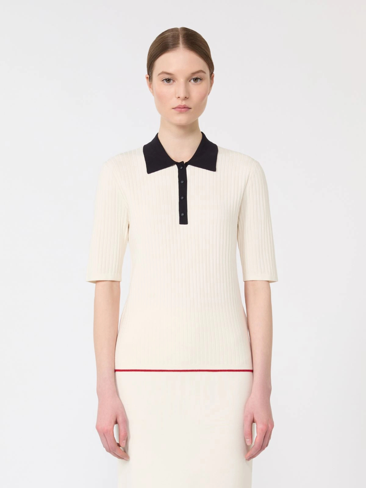 Woman wearing a cream dress with black collar and red trim on a white background