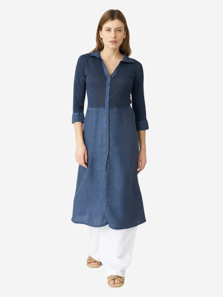 A woman wearing a navy 3/4 sleeve midi shirt dress with a collar and button-up closure, paired with white pants.