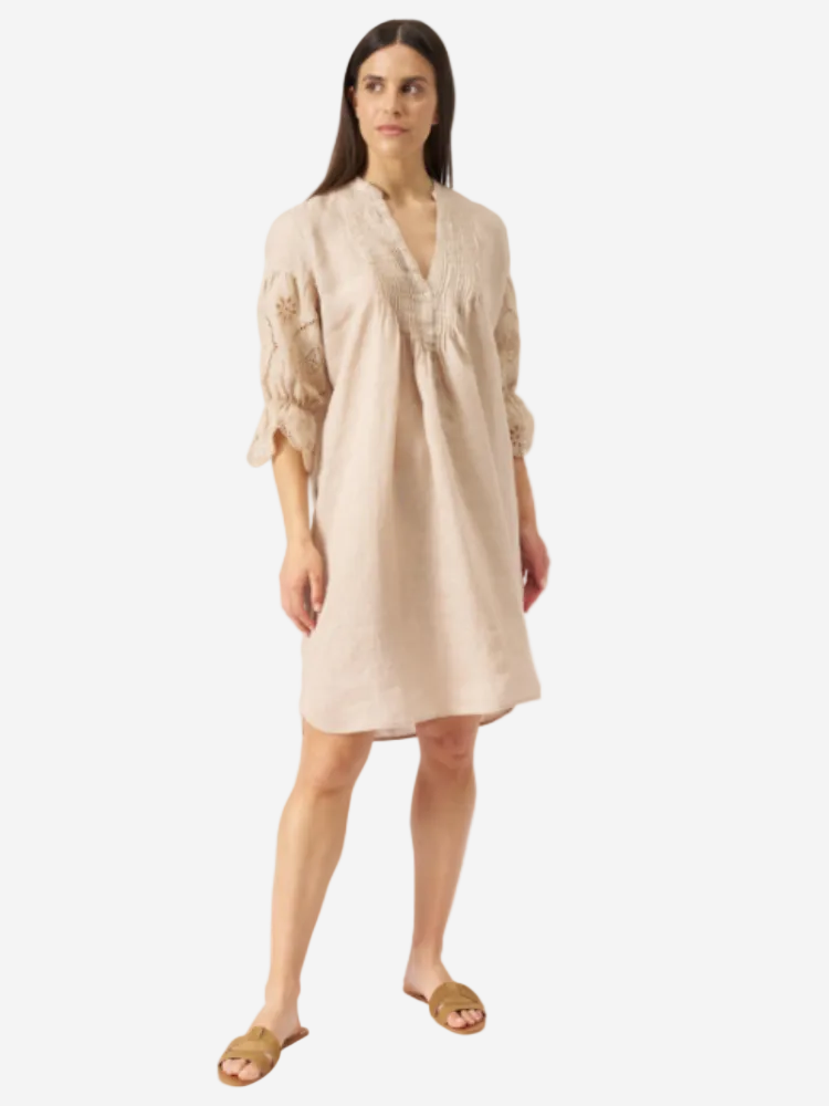 A woman standing and wearing an ecru-colored, v-neck, 3/4 sleeve short dress with embroidered detailing.
