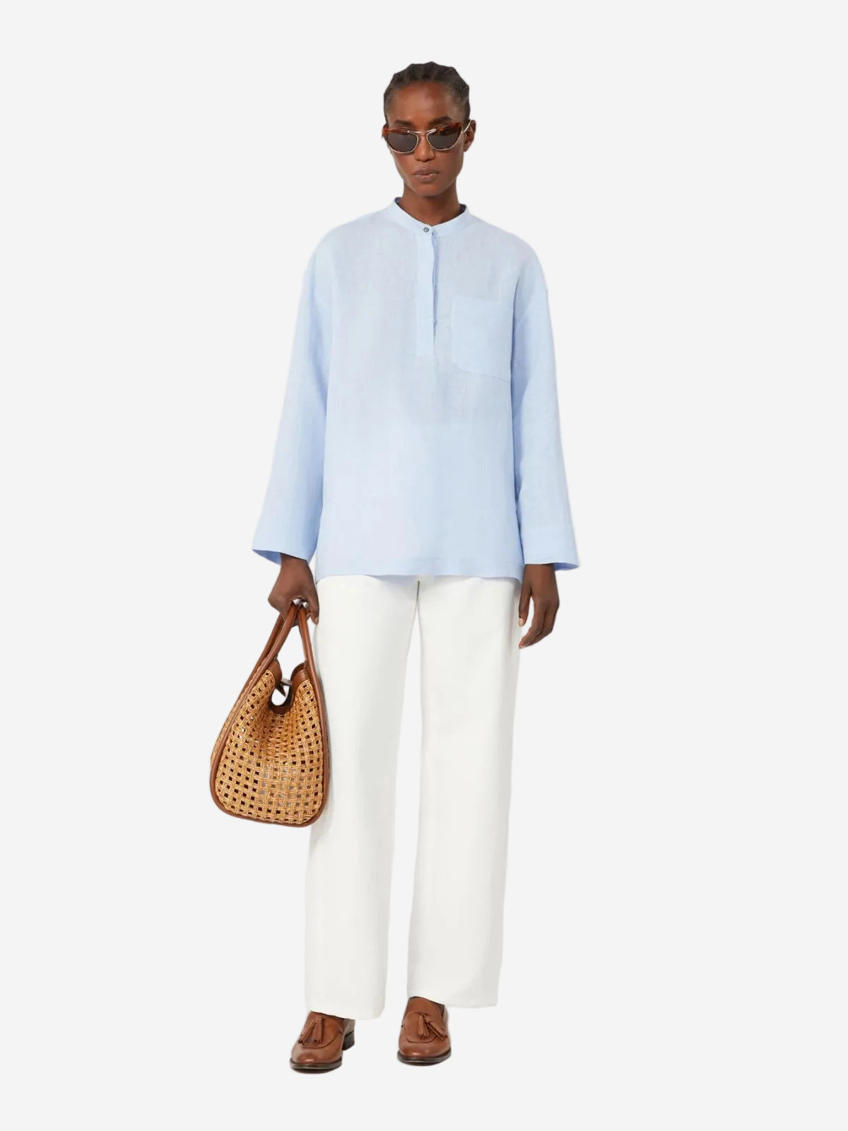 Person wearing a light blue shirt and white pants, holding a woven bag on a white background