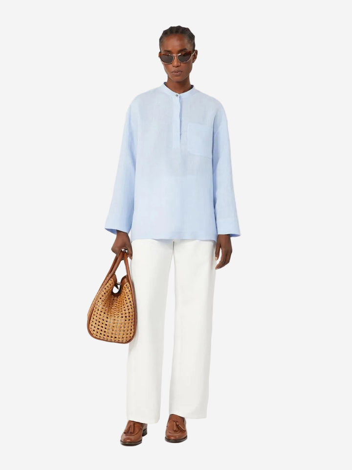 Person wearing a light blue shirt and white pants, holding a woven bag on a white background