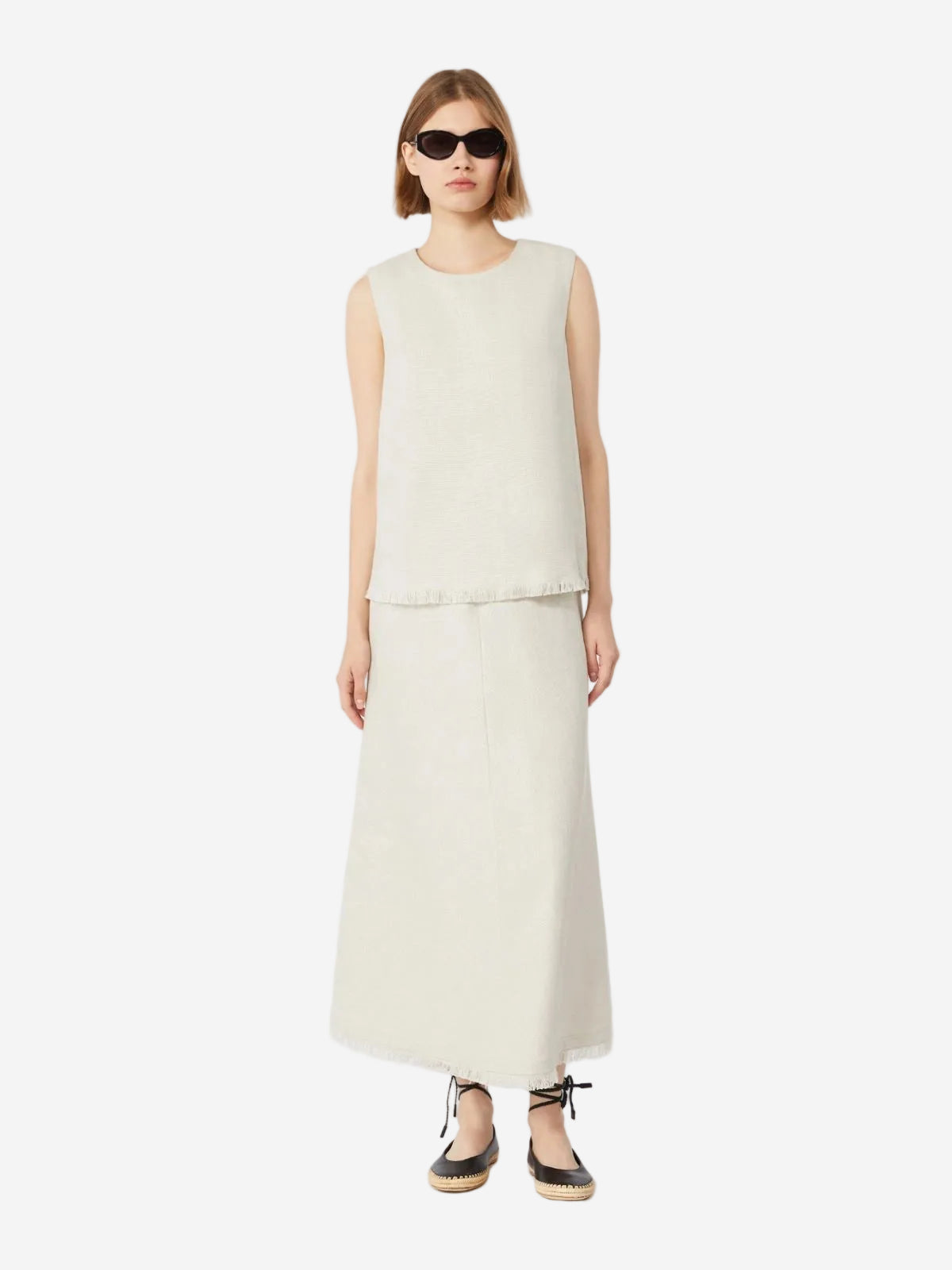 Woman wearing a sleeveless beige top and long skirt on a white background