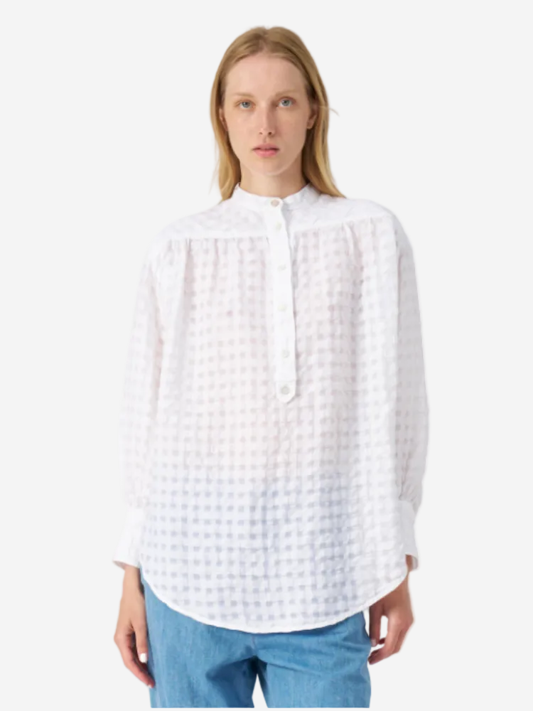 A woman wearing a long sleeve, half button-up white blouse with a geometric pattern, paired with blue jeans.