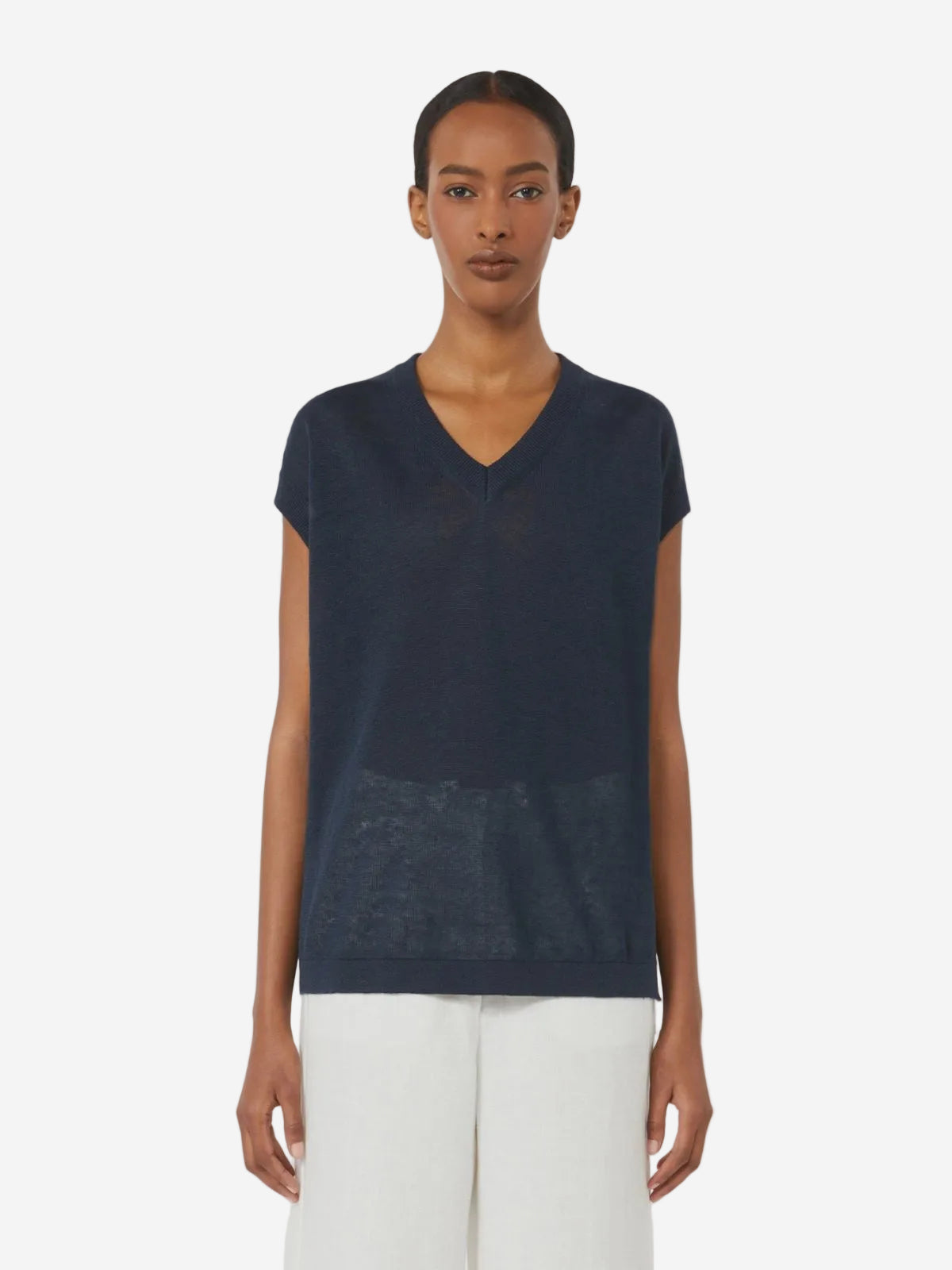Woman wearing a navy blue sleeveless top and white pants on a white background