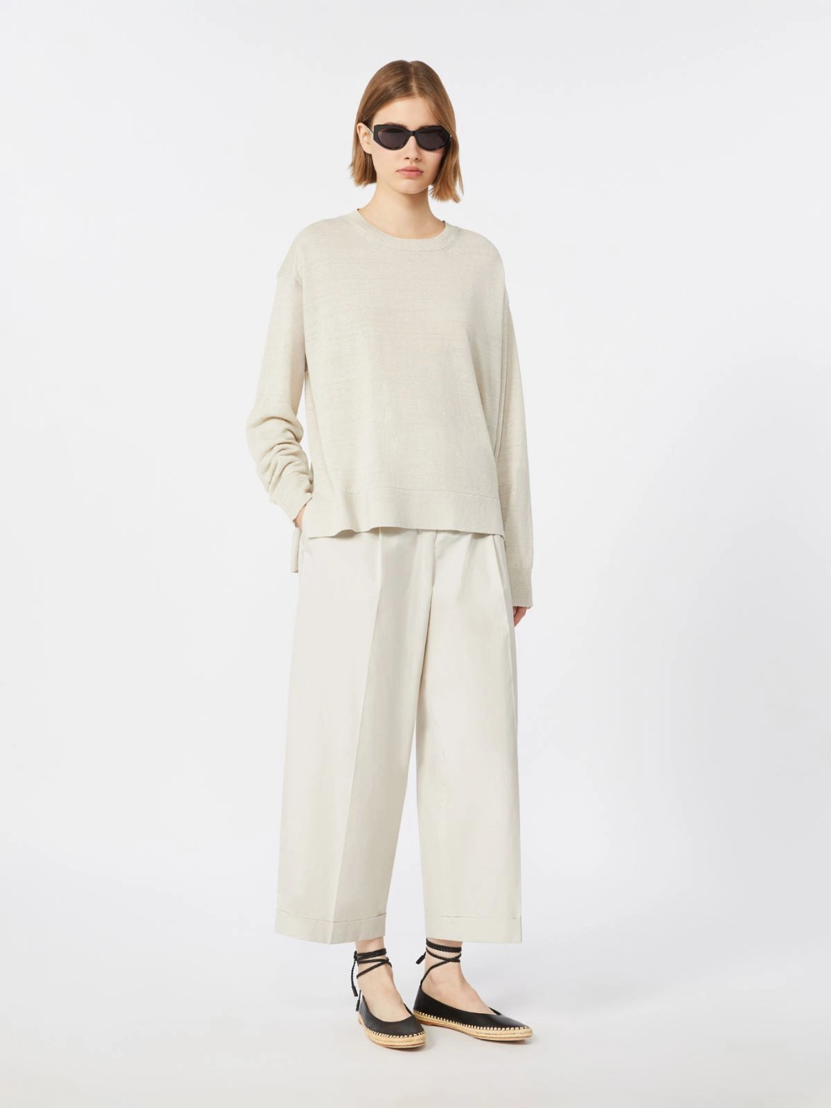 Person wearing a beige long-sleeve top and white pants on a white background