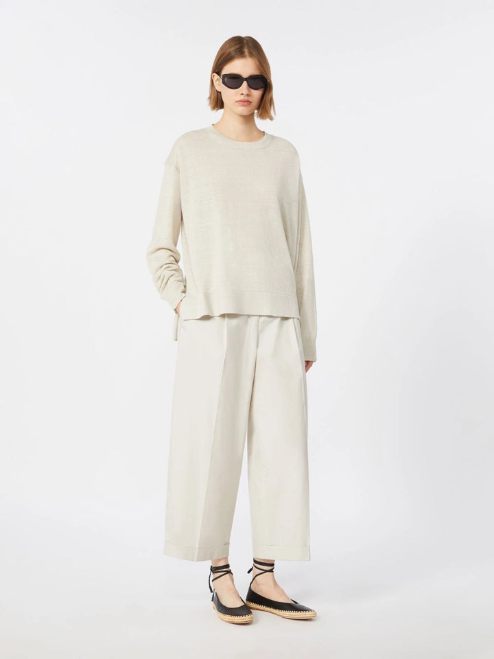 Person wearing a beige long-sleeve top and white pants on a white background