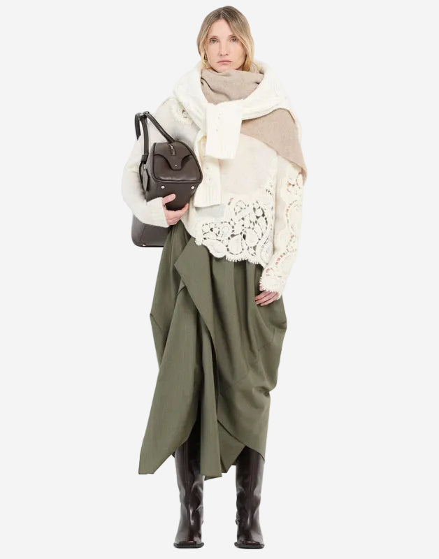 Woman wearing a green dress, white sweater, and brown boots against a white background