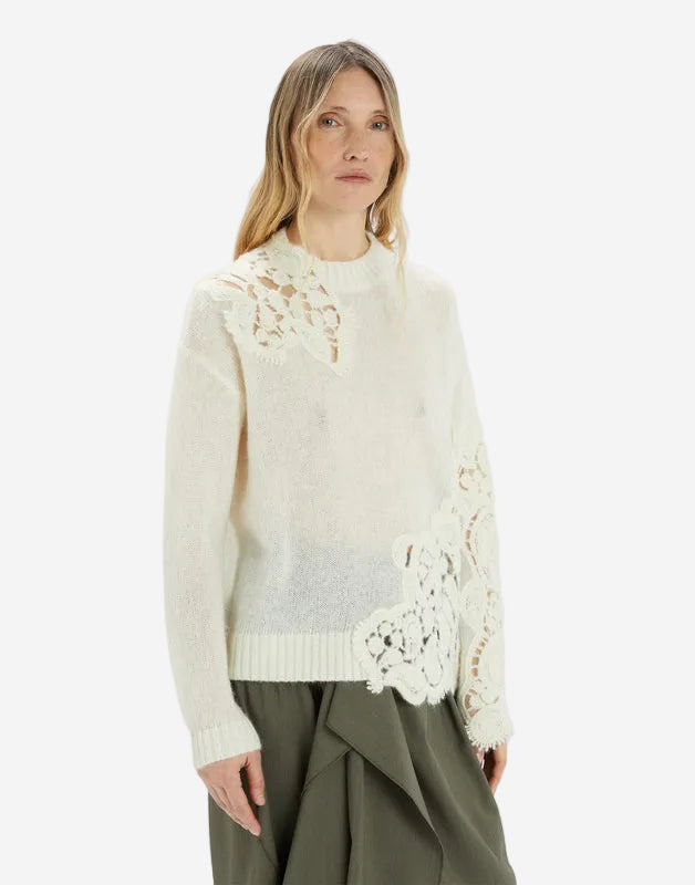 Woman wearing a cream-colored sweater with lace details on a white background