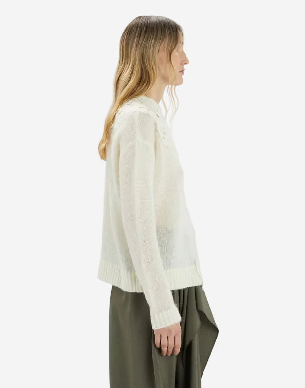 Woman wearing a white sweater and green pants on a light gray background