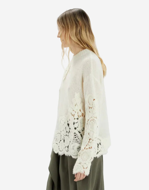 Woman wearing a white lace-sleeve top against a plain background
