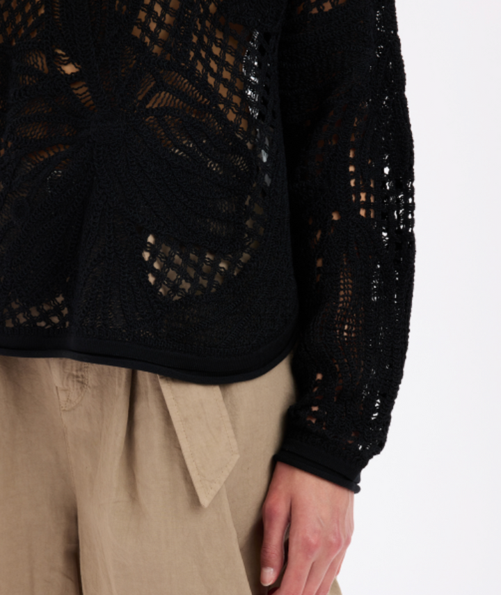 Black lace top worn by a person with beige pants on a white background