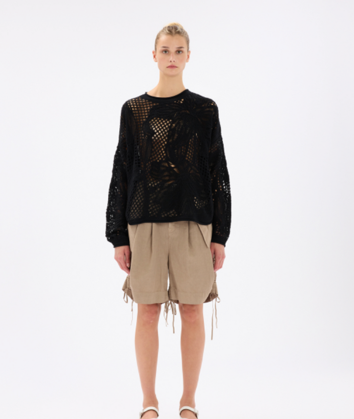 Person wearing a black textured sweater and beige shorts on a white background