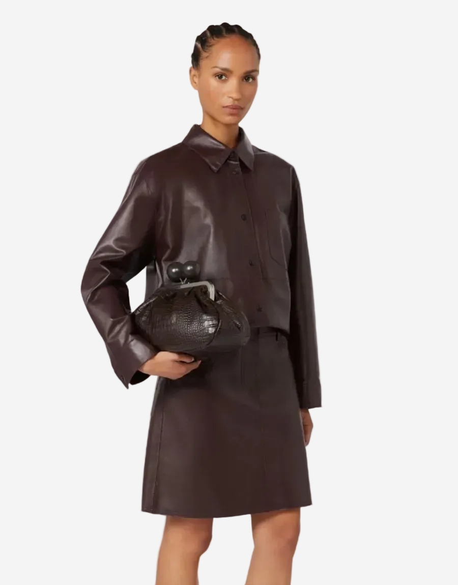 Woman wearing a brown leather outfit holding a matching handbag on a white background