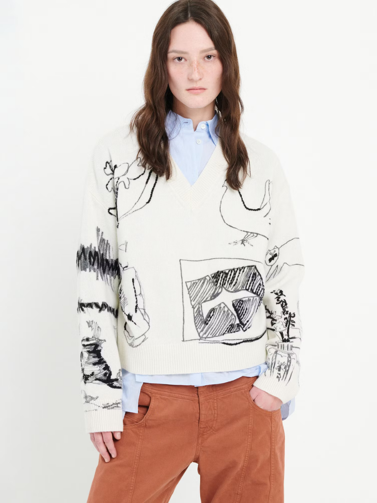 Person wearing a white sweater with black and gray abstract designs on a plain background