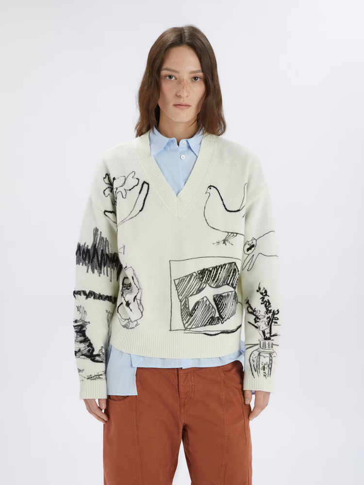 Person wearing a cream-colored sweater with black abstract designs on a white background