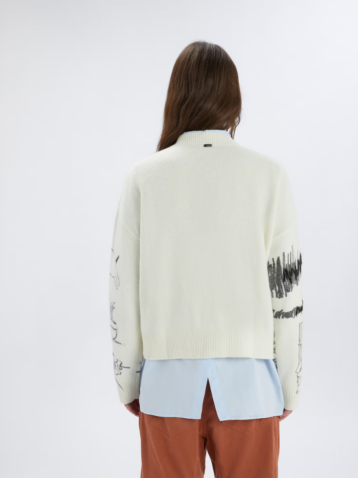 Person wearing a cream-colored cardigan with black text pattern on sleeves against a white background