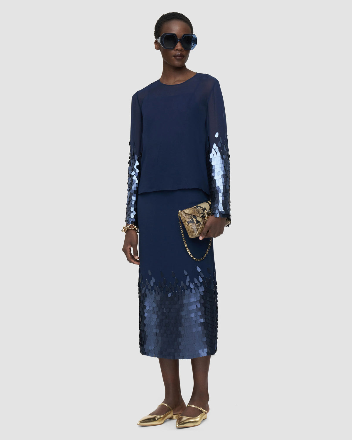 Model wearing the JOSEPH Ariane navy sequin sleeve blouse with a matching sequin-hem midi skirt and gold flats