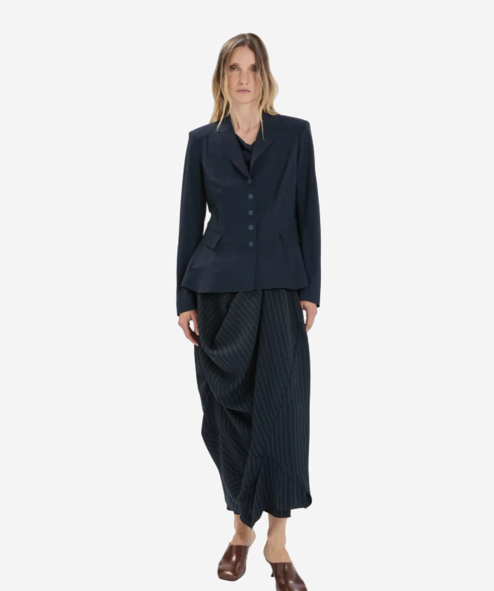 Woman wearing a dark blue suit with a draped skirt on a white background