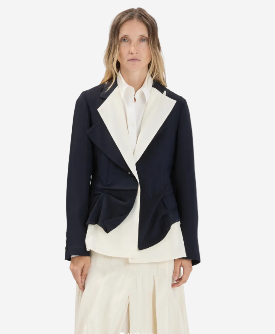 Woman wearing a black blazer over a white shirt and pants on a light gray background