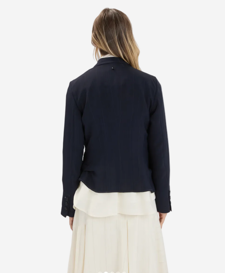 Person wearing a black blazer over a white dress on a plain background