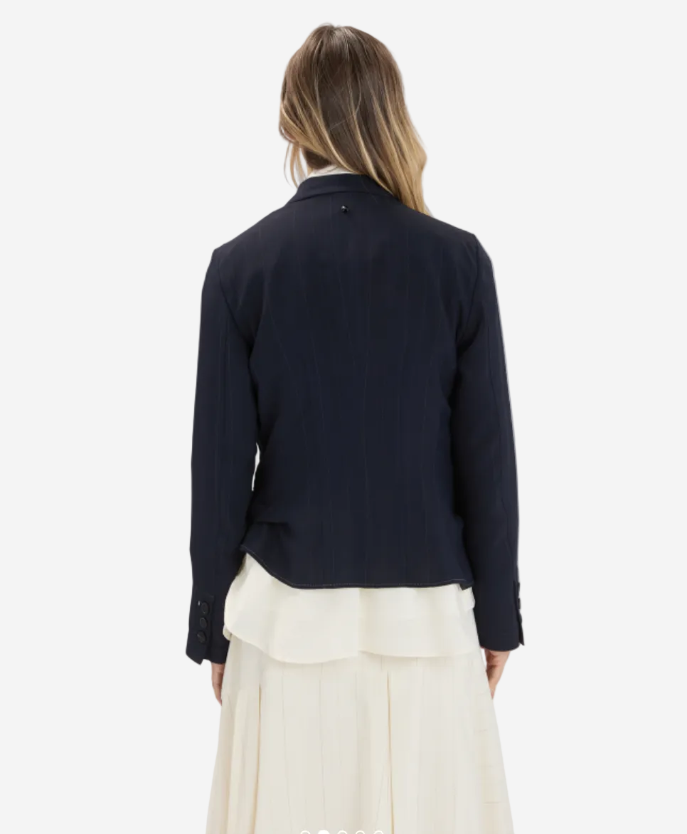 Person wearing a black blazer over a white dress on a plain background