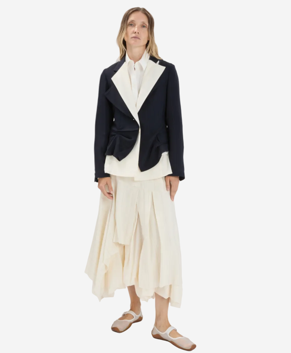 Woman wearing a black blazer with a white shirt and cream skirt on a white background