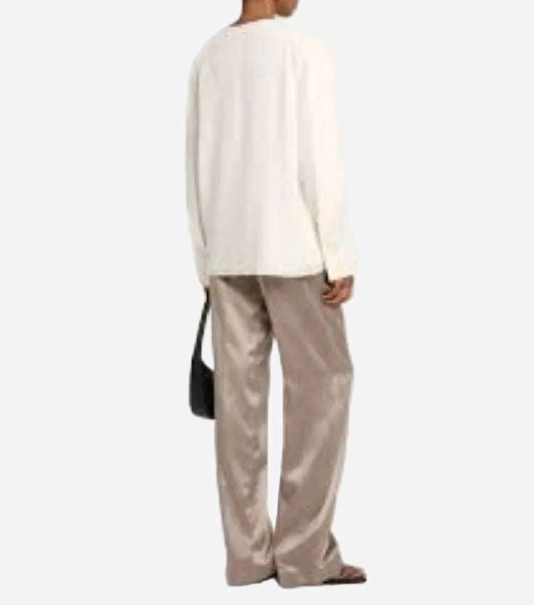 Person wearing a cream sweater and beige pants with a black handbag on a white background