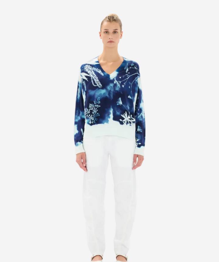 Woman wearing a blue tie-dye sweater and white pants on a white background