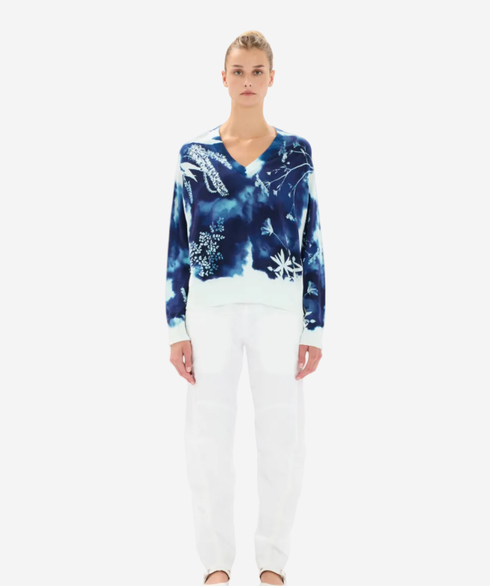 Woman wearing a blue tie-dye sweater and white pants on a white background