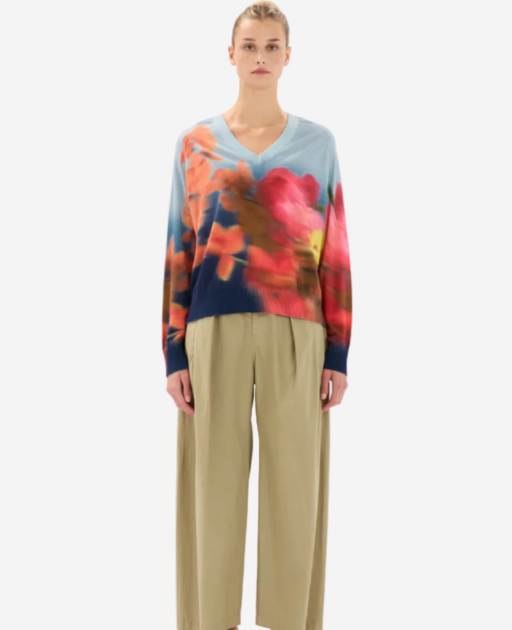 Person wearing a colorful tie-dye sweater and beige pants on a white background