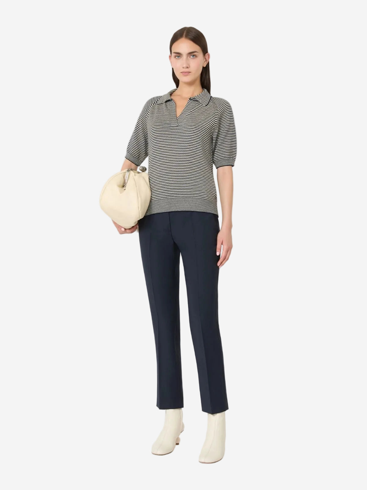 Woman wearing a striped shirt and navy pants with white boots on a white background