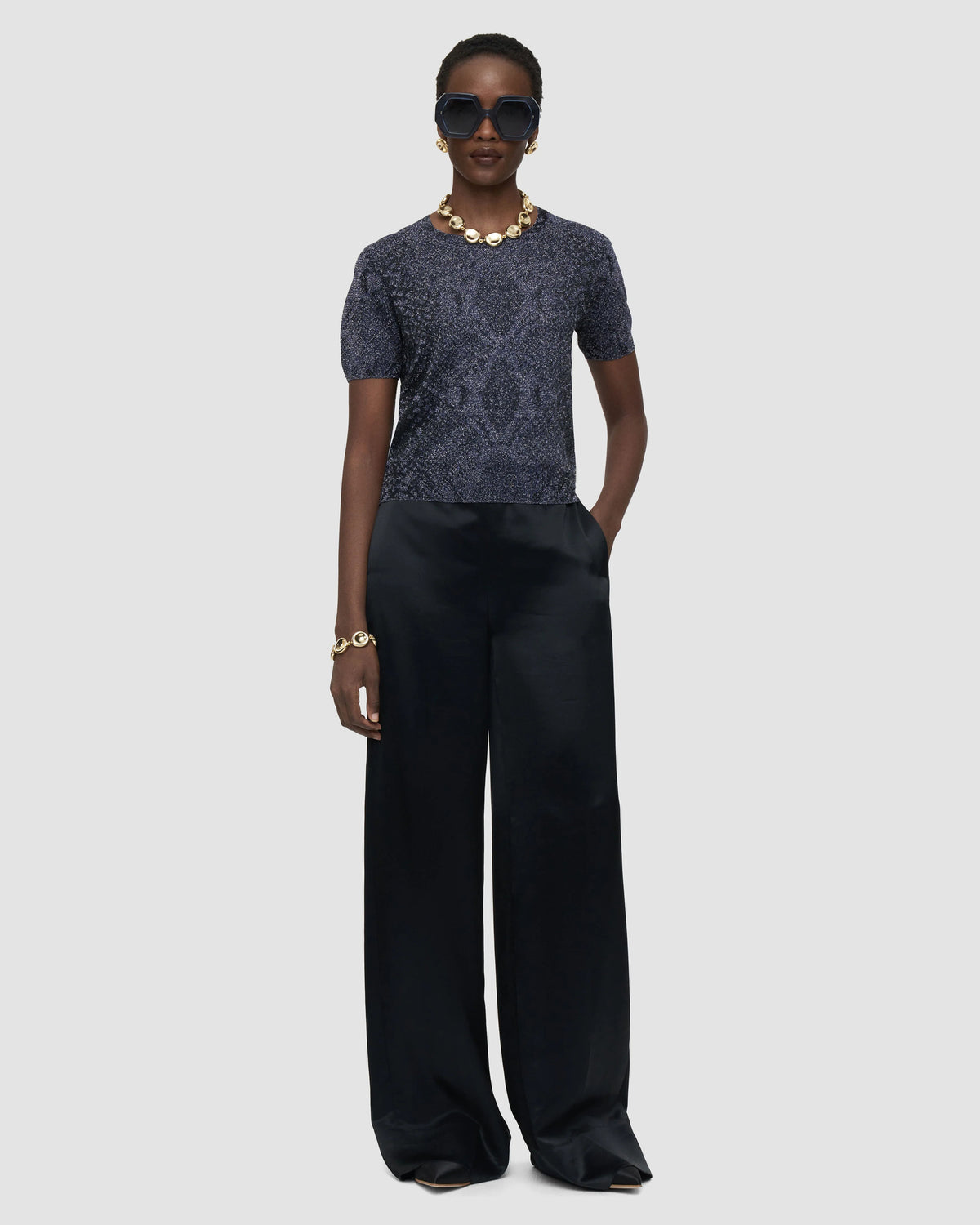 Model wearing the JOSEPH Char short-sleeve metallic knit top with black satin wide-leg trousers