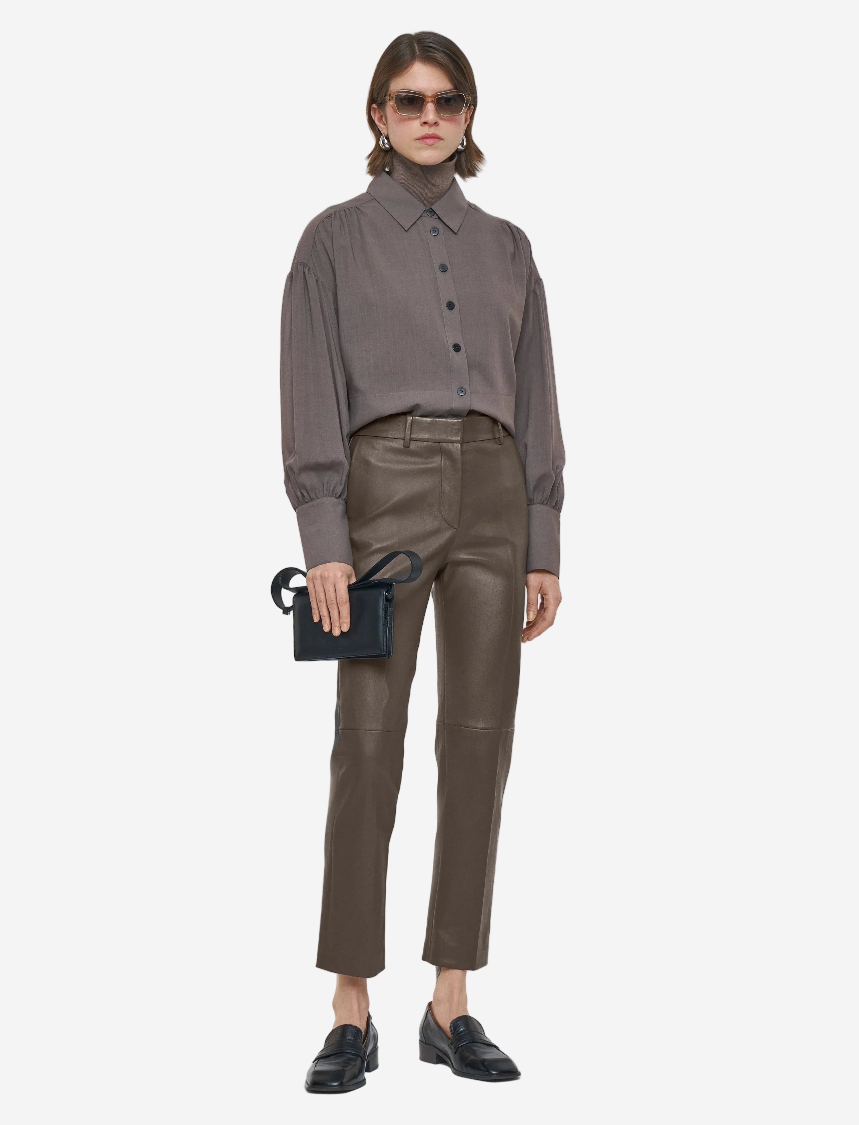 Person wearing a gray shirt and brown leather pants on a white background