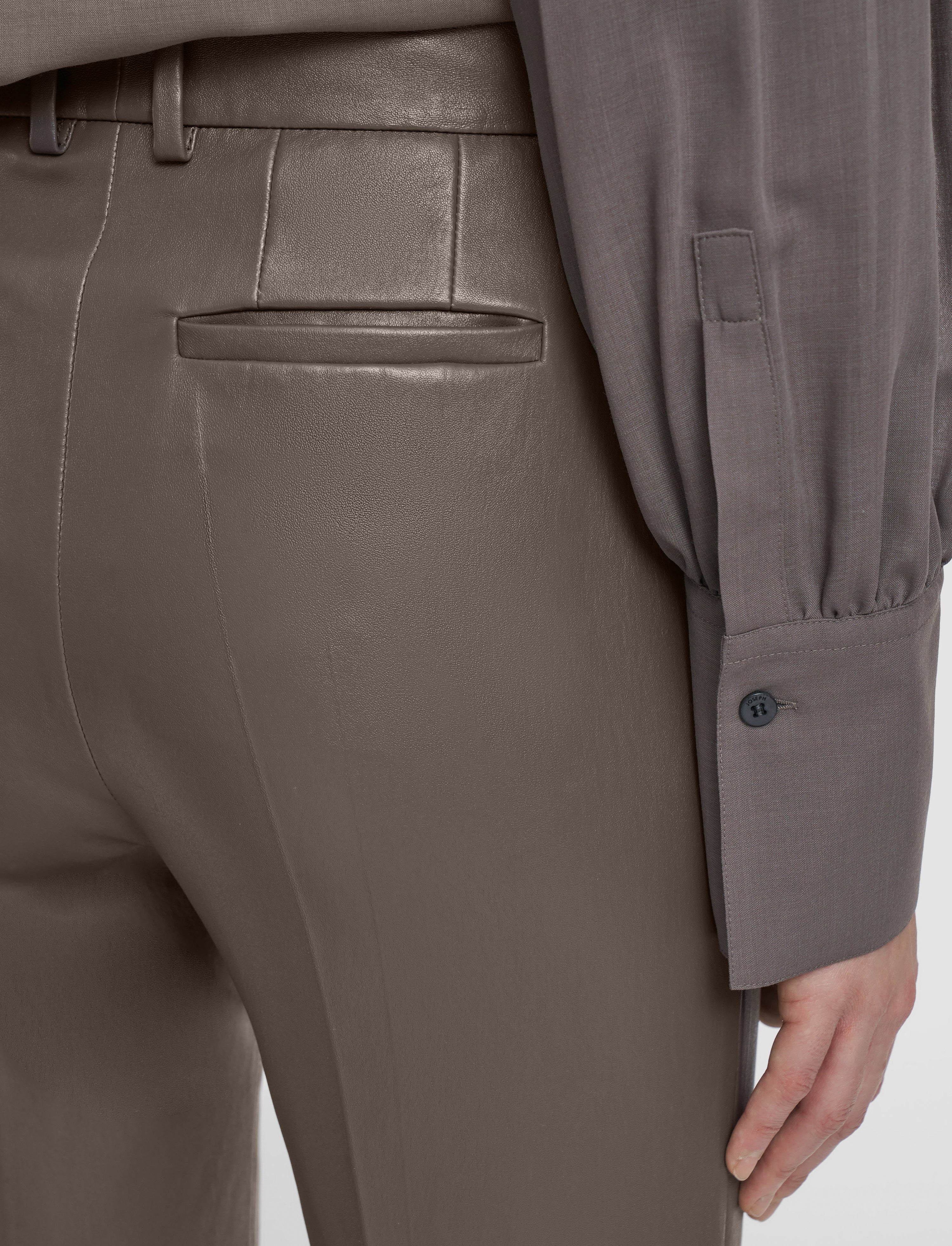 Close-up of a person wearing brown pants and a gray shirt with a button.