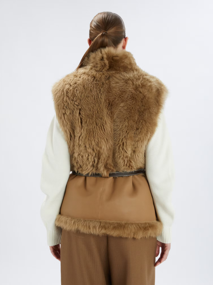 Person wearing a brown fur vest over a white shirt and beige pants on a white background