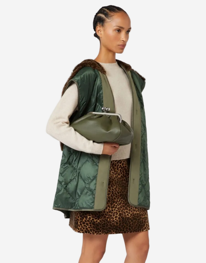 Woman wearing a green vest over a white sweater and leopard print skirt, holding a green bag.