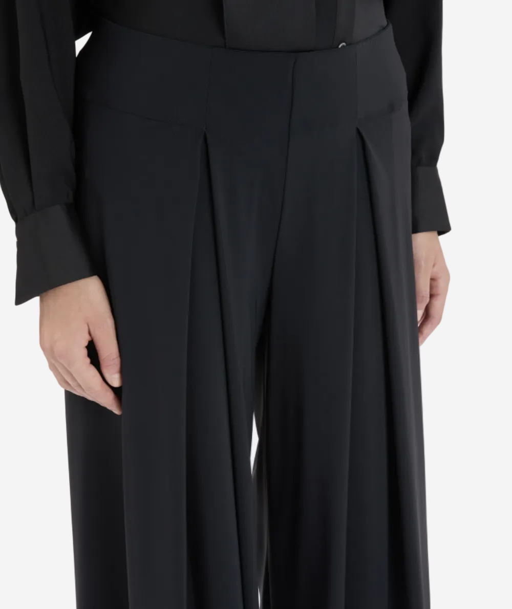 Person wearing a black suit with wide-leg pants on a light gray background