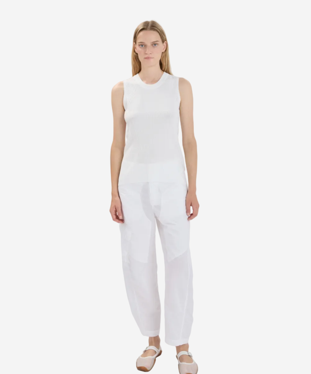 Woman wearing a white sleeveless top and pants on a plain background