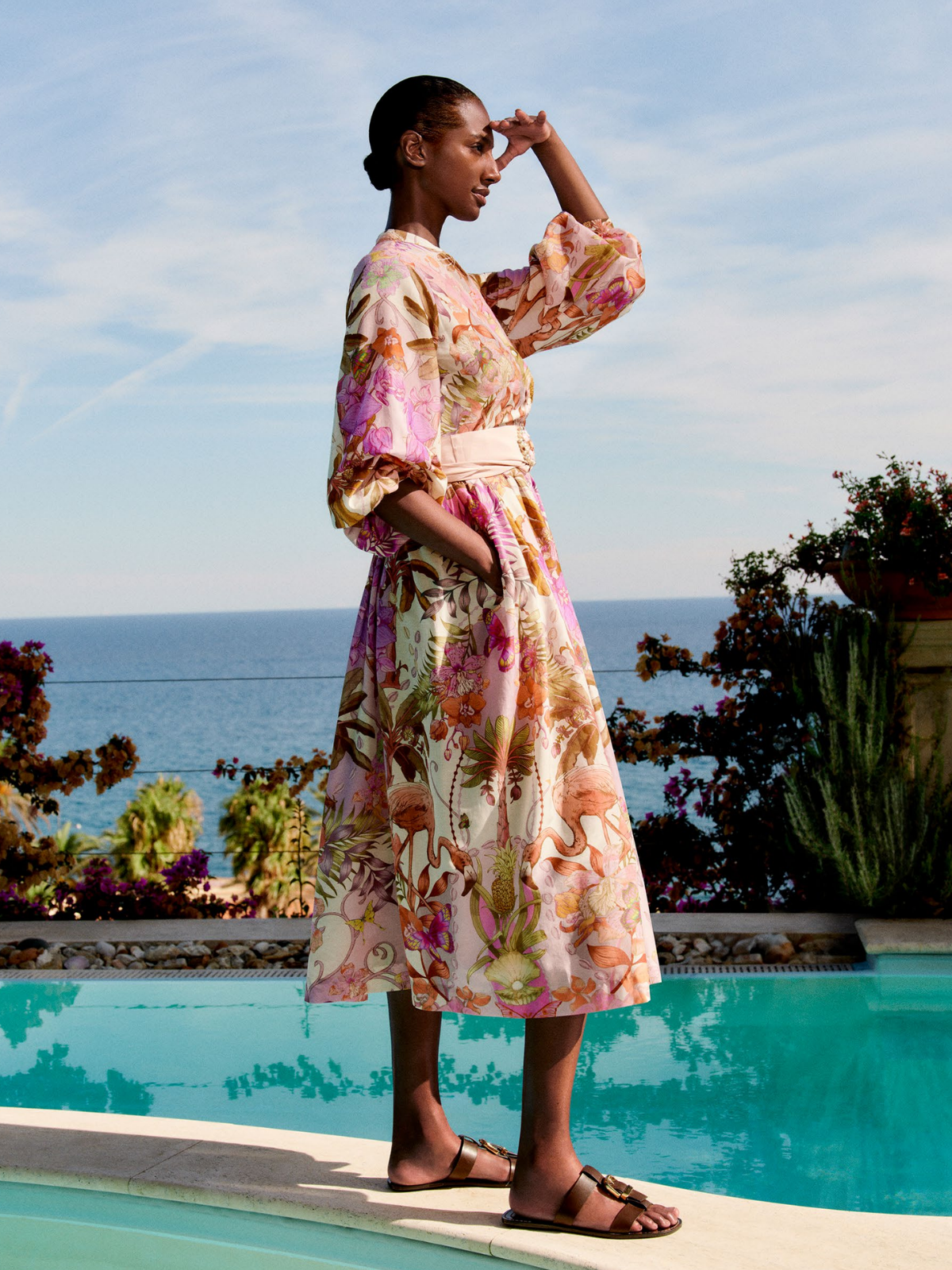 Woman in a floral dress standing by a pool with ocean view