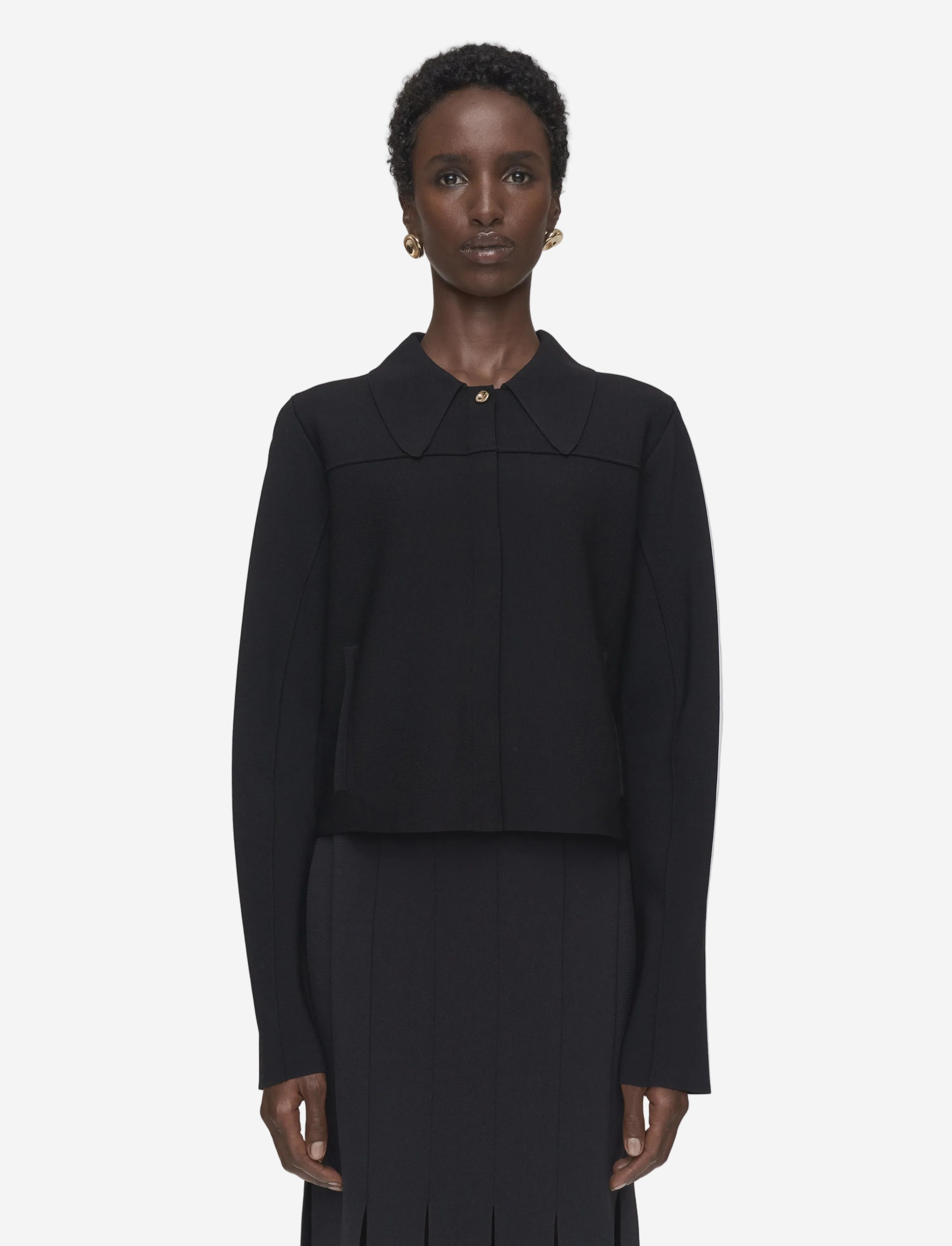Person wearing a black outfit with a high collar on a plain background