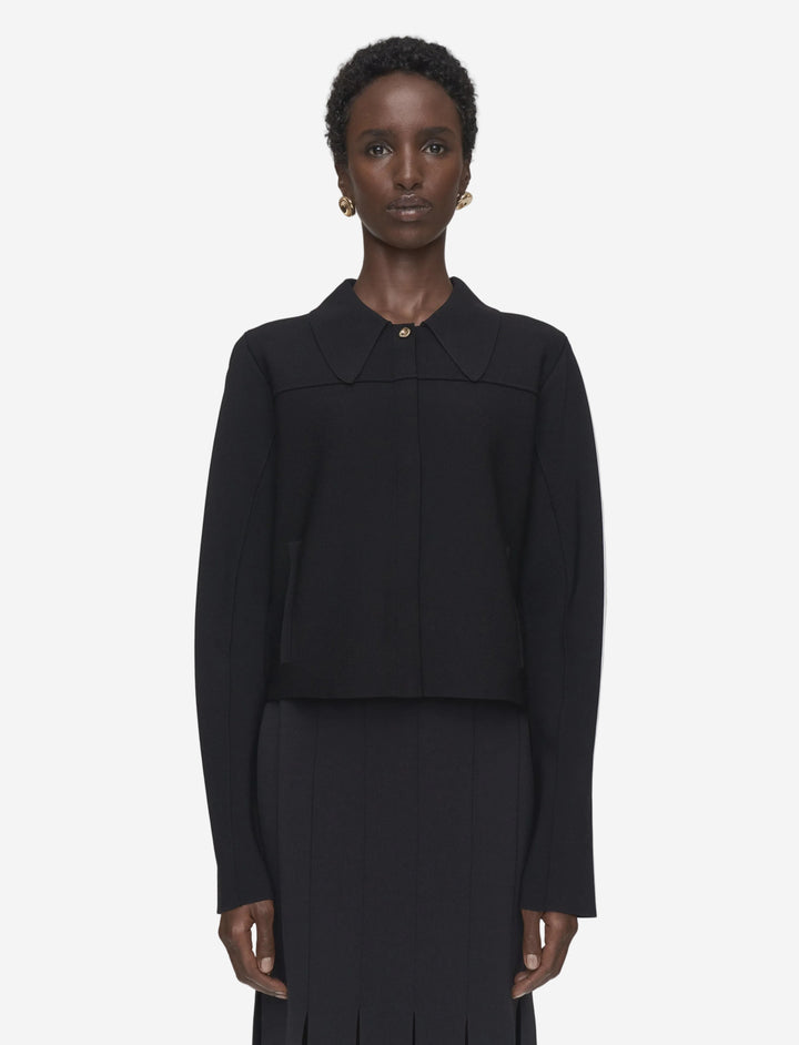 Person wearing a black outfit with a high collar on a plain background