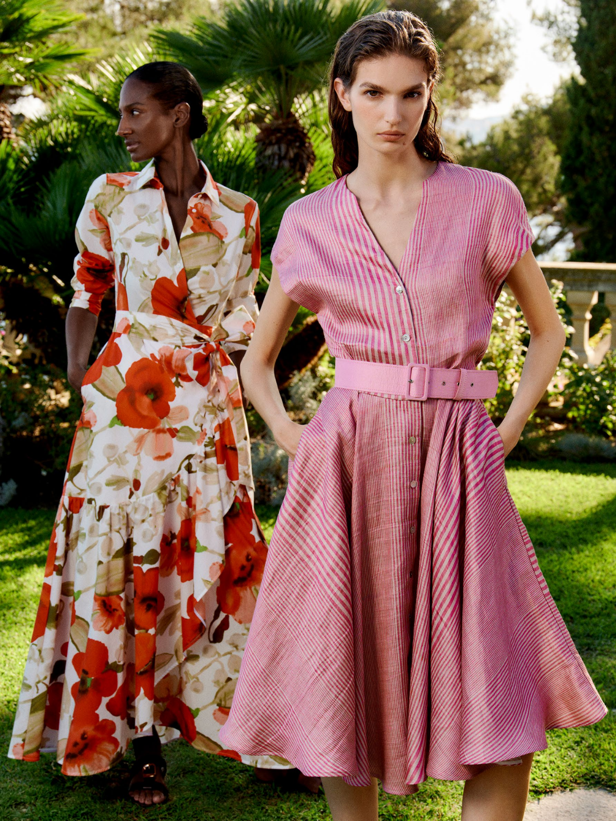 Two women wearing floral and pink dresses standing outdoors with greenery in the background