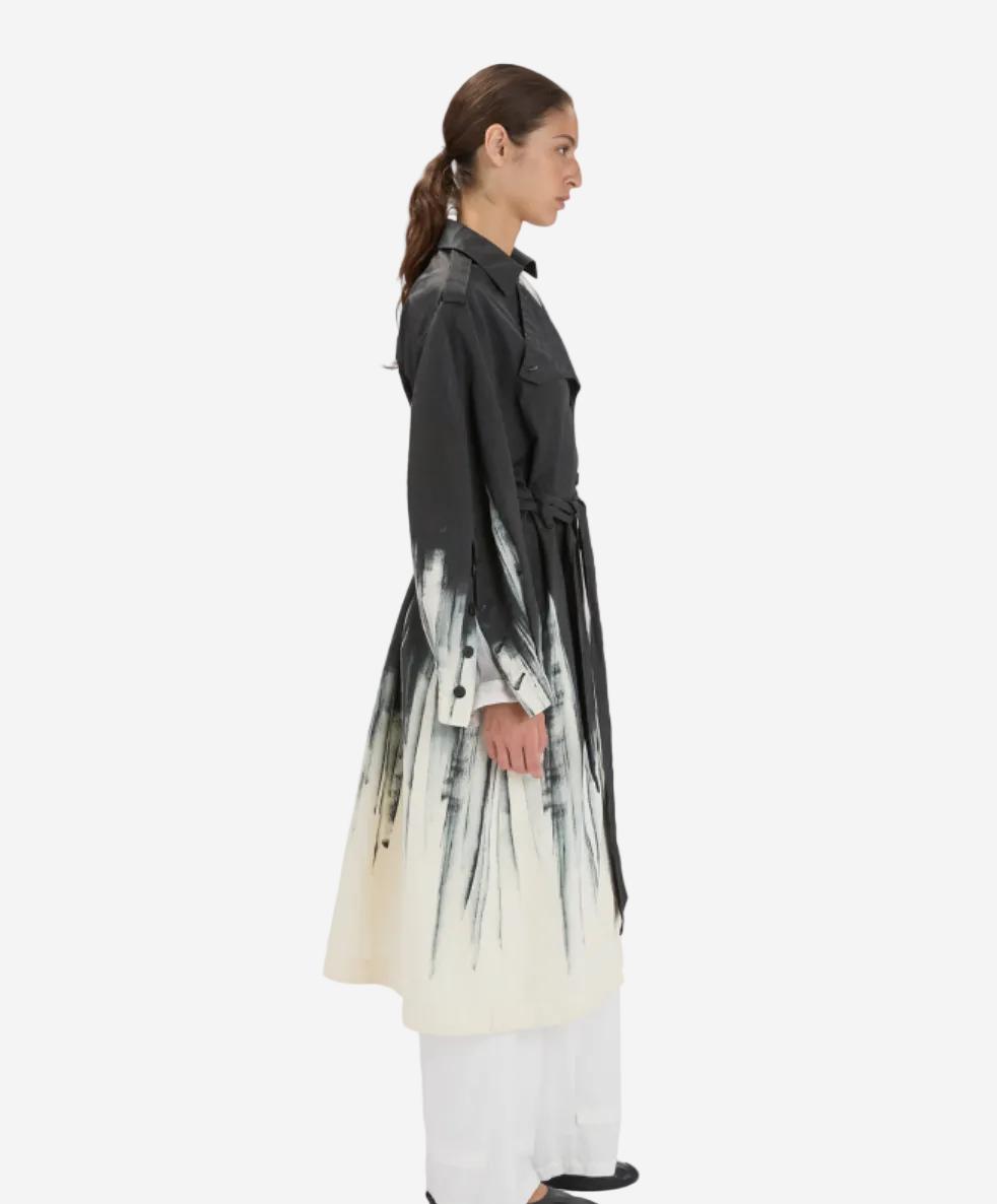 Woman wearing a long, dark coat with a white and black abstract pattern on a white background